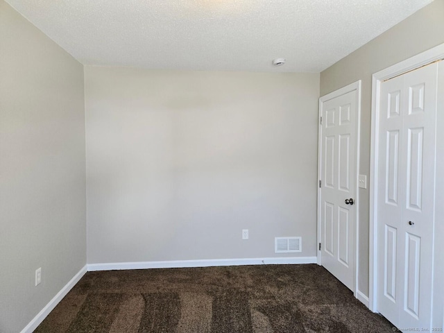 empty room with baseboards, visible vents, dark carpet, and a textured ceiling