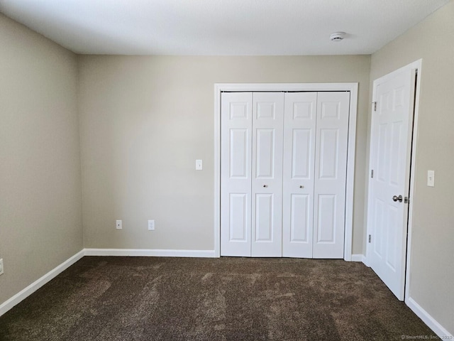 unfurnished bedroom featuring baseboards, dark colored carpet, and a closet