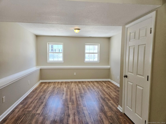 unfurnished room featuring dark wood-style flooring, a textured ceiling, and baseboards