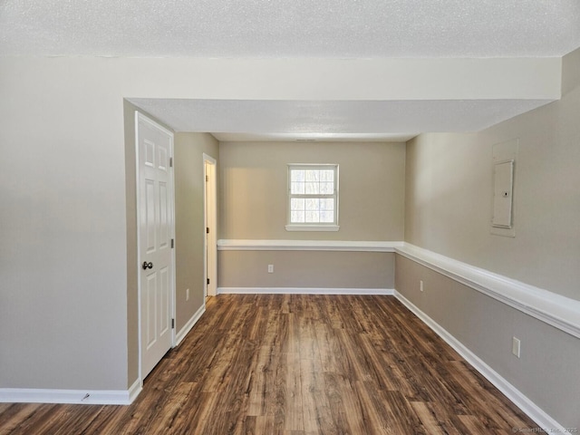 spare room featuring electric panel, dark wood finished floors, a textured ceiling, and baseboards