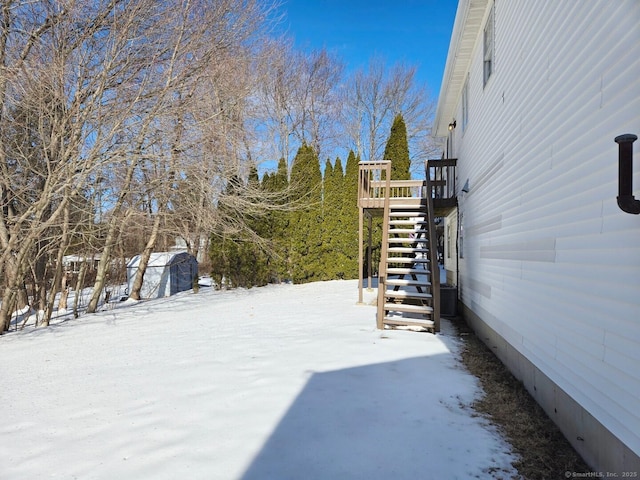 yard layered in snow with a storage shed, stairway, and an outdoor structure