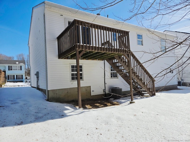 snow covered rear of property with a deck, central AC unit, and stairs