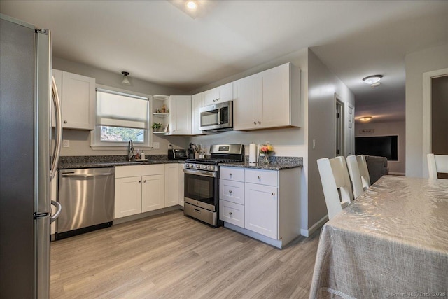 kitchen featuring dark stone counters, appliances with stainless steel finishes, light wood-style floors, white cabinets, and a sink