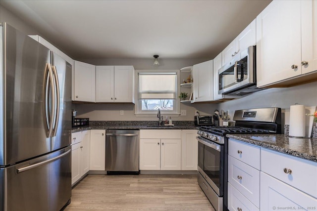 kitchen with white cabinetry, dark stone countertops, appliances with stainless steel finishes, and a sink