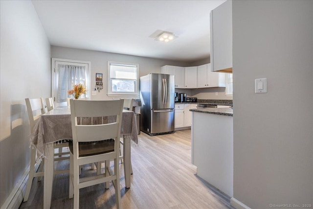 kitchen featuring light wood-style flooring, white cabinets, dark stone counters, and freestanding refrigerator