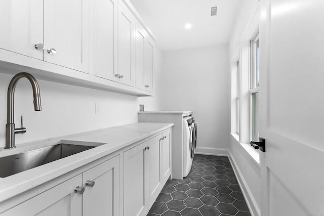 laundry area with washing machine and clothes dryer, cabinet space, a sink, dark tile patterned flooring, and baseboards