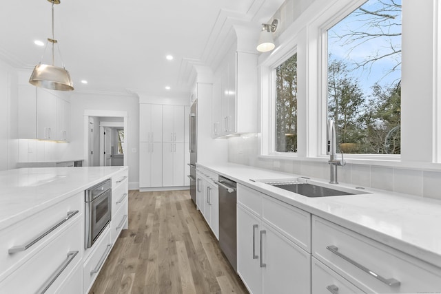 kitchen featuring stainless steel appliances, backsplash, light wood-style flooring, white cabinets, and a sink