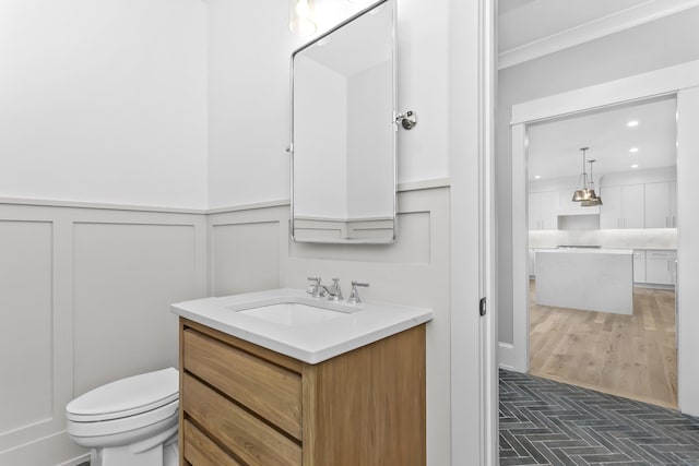 bathroom with recessed lighting, a decorative wall, toilet, wainscoting, and vanity