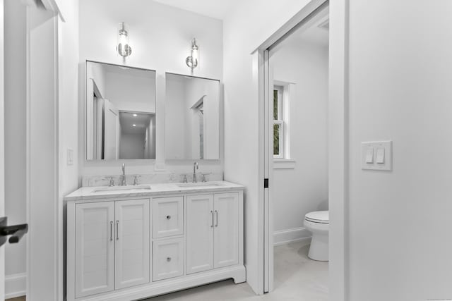 full bath with toilet, double vanity, baseboards, and a sink