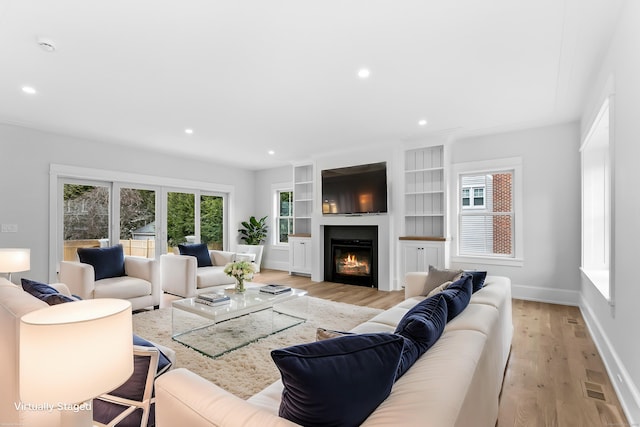 living area featuring baseboards, a lit fireplace, light wood-style flooring, and recessed lighting