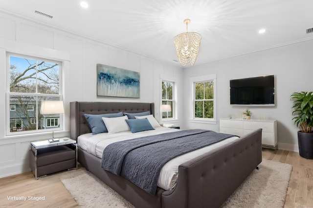 bedroom featuring ornamental molding, light wood finished floors, visible vents, and a decorative wall