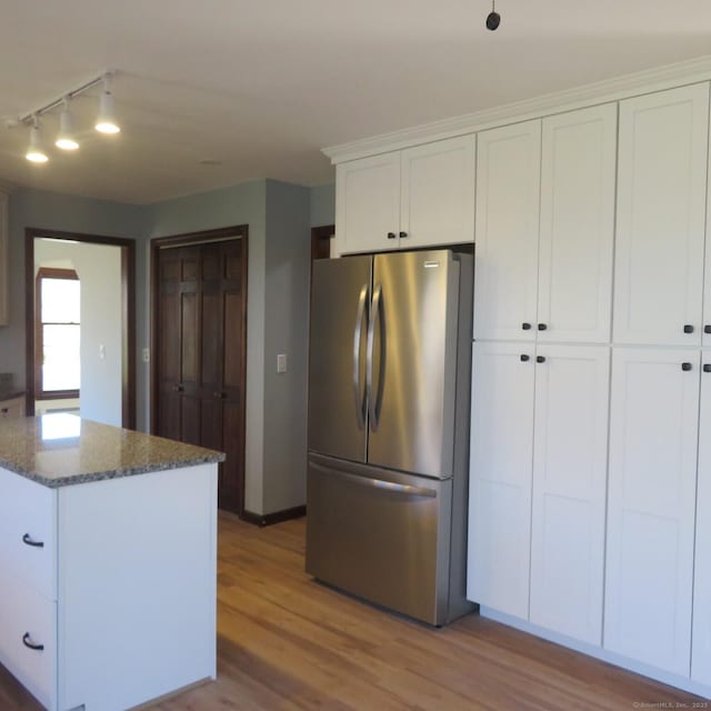 kitchen featuring dark stone counters, white cabinets, wood finished floors, and freestanding refrigerator