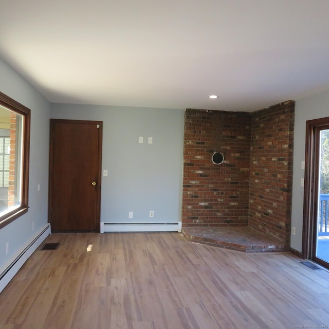 empty room featuring a baseboard heating unit, baseboards, visible vents, and wood finished floors