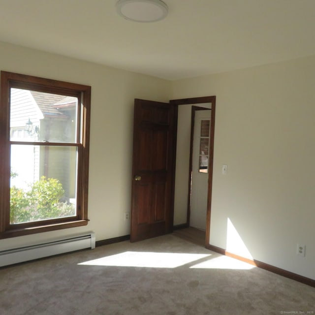 spare room featuring baseboard heating, light colored carpet, and baseboards