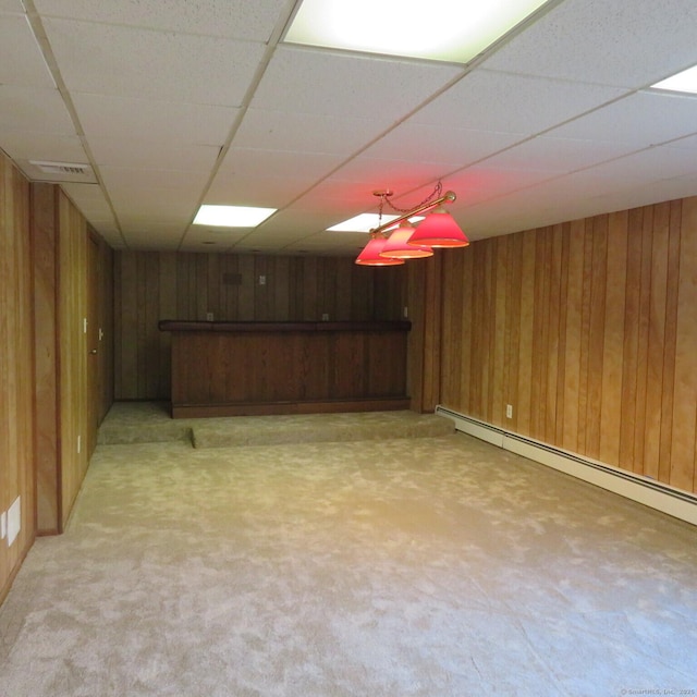 finished below grade area with a drop ceiling, a baseboard radiator, wooden walls, and light colored carpet