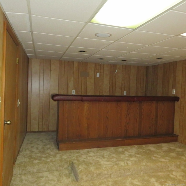 bar with light carpet, wood walls, and a paneled ceiling