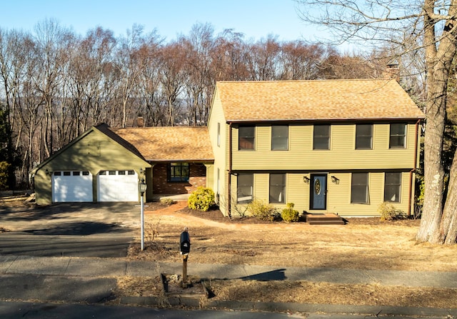 colonial-style house with aphalt driveway, an attached garage, a chimney, and a shingled roof