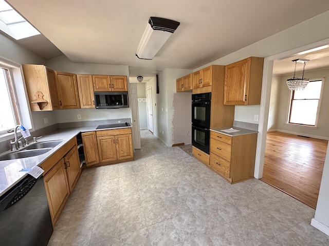 kitchen with a skylight, light countertops, a sink, black appliances, and baseboards