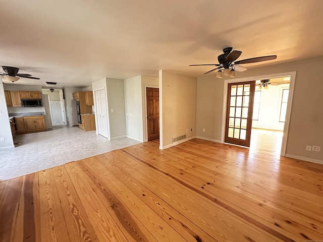 unfurnished living room with light wood-type flooring, baseboards, visible vents, and a ceiling fan