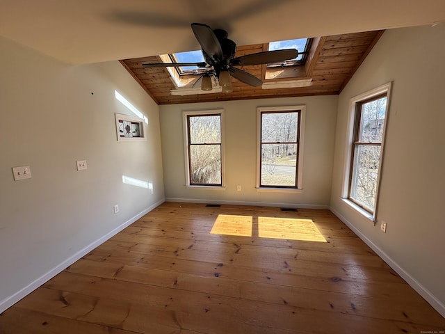 empty room with visible vents, vaulted ceiling with skylight, light wood-style flooring, and baseboards