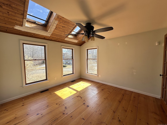 empty room featuring lofted ceiling with skylight, baseboards, visible vents, and hardwood / wood-style flooring