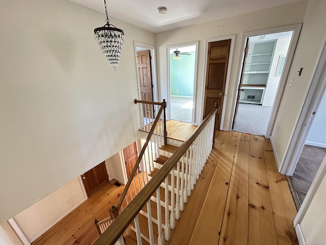 hallway featuring light wood-style flooring, a chandelier, baseboards, and an upstairs landing