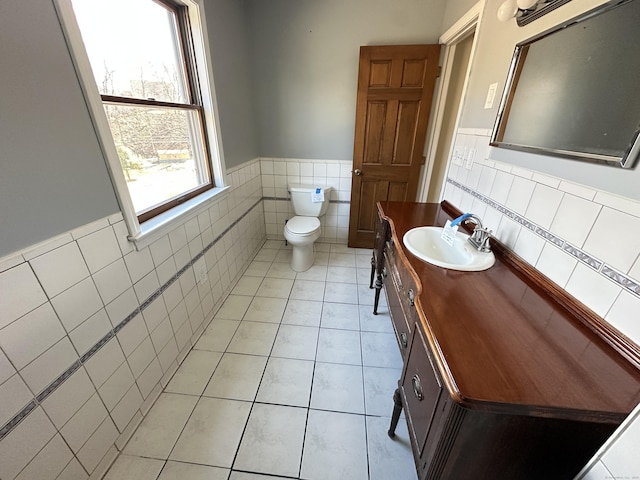 bathroom with wainscoting, toilet, tile patterned flooring, vanity, and tile walls