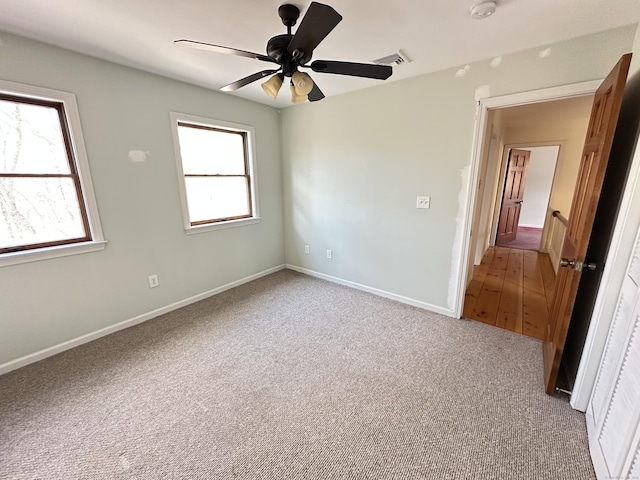 carpeted spare room with a healthy amount of sunlight, ceiling fan, visible vents, and baseboards