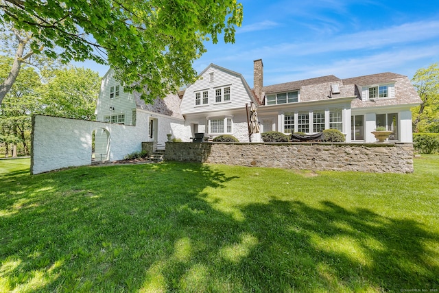 rear view of house featuring a yard, a gambrel roof, and a chimney