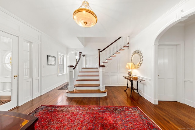 foyer entrance with arched walkways, stairway, a decorative wall, and wood finished floors