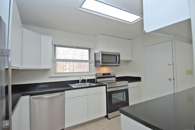 kitchen featuring light tile patterned floors, stainless steel appliances, a sink, white cabinets, and dark countertops