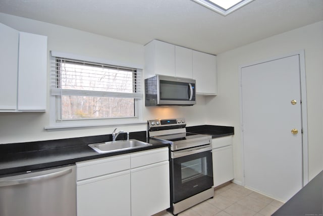 kitchen with light tile patterned floors, dark countertops, stainless steel appliances, white cabinetry, and a sink