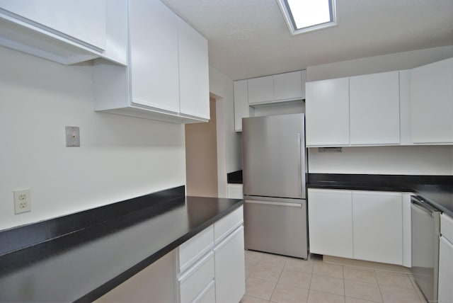 kitchen with light tile patterned floors, appliances with stainless steel finishes, dark countertops, and white cabinetry