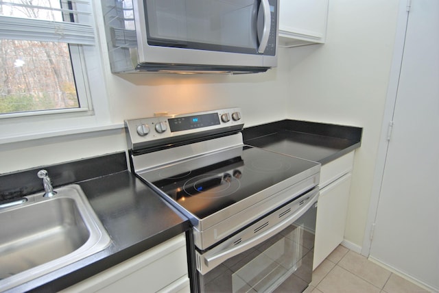 kitchen featuring light tile patterned floors, stainless steel appliances, dark countertops, white cabinetry, and a sink