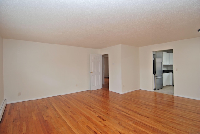 empty room with a baseboard radiator, baseboards, light wood-style flooring, and a textured ceiling