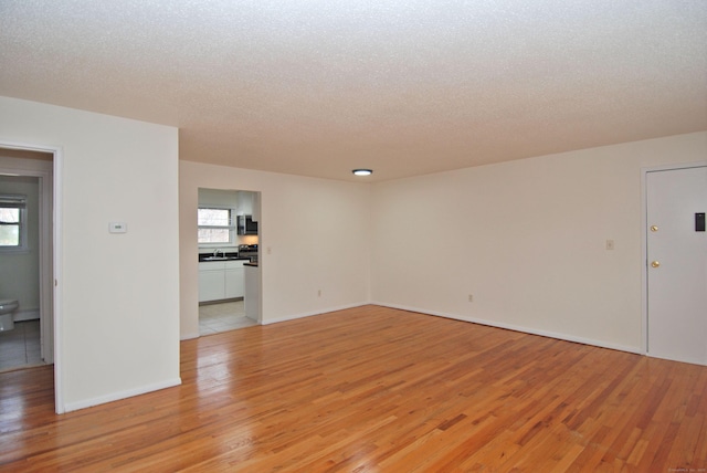 unfurnished room with light wood-type flooring, a healthy amount of sunlight, and a textured ceiling