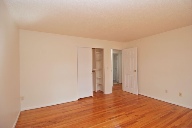 empty room with a textured ceiling, baseboards, and light wood-style floors