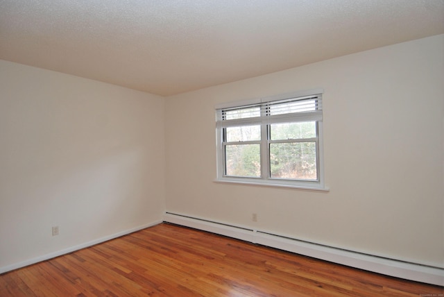 empty room with a baseboard heating unit, baseboards, and wood finished floors