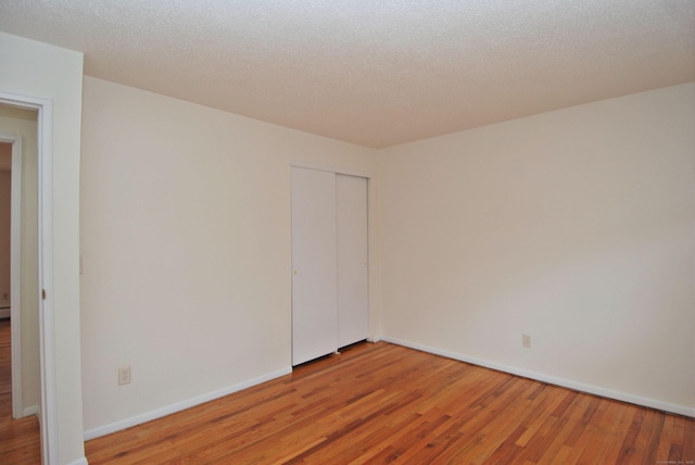 spare room with light wood finished floors, baseboards, and a textured ceiling