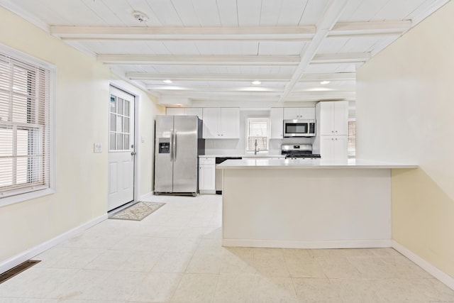 kitchen with a peninsula, a sink, appliances with stainless steel finishes, white cabinetry, and beamed ceiling