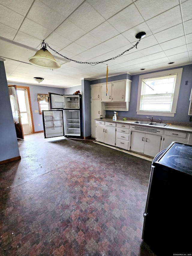 kitchen with baseboards, a sink, light countertops, white cabinets, and range