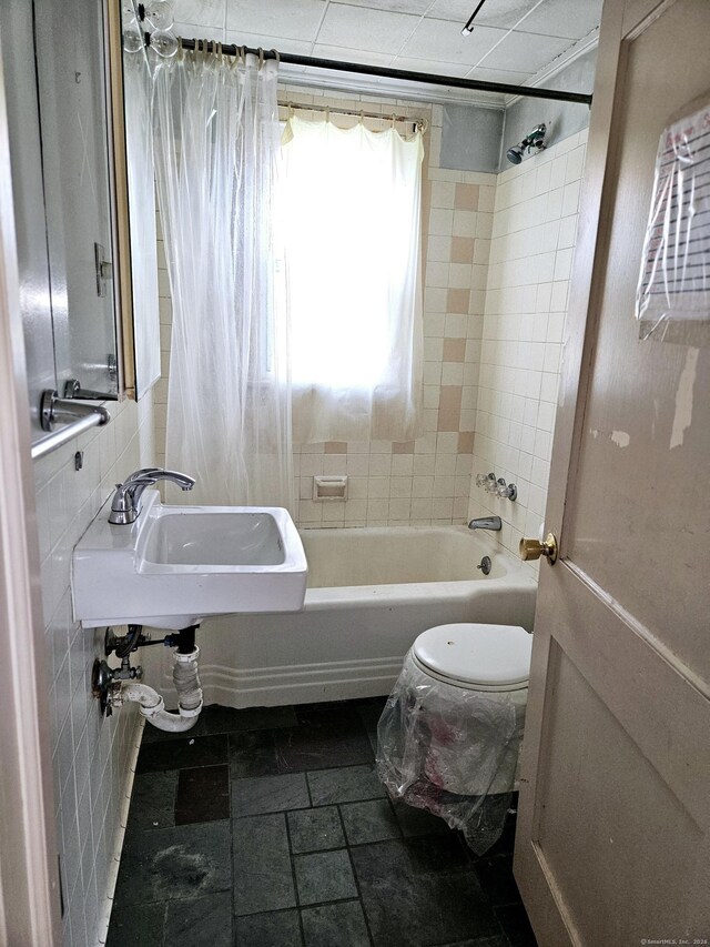 bathroom with a sink, toilet, tile walls, and shower / bathtub combination