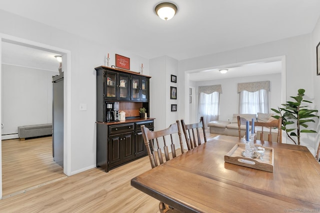 dining room featuring baseboards, bar area, light wood-style floors, a baseboard heating unit, and a barn door