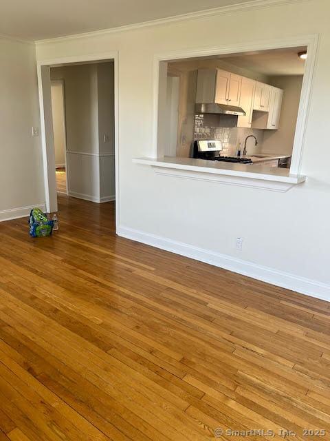 unfurnished living room with a sink, crown molding, baseboards, and wood finished floors