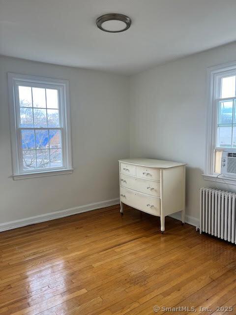 unfurnished bedroom featuring baseboards, light wood finished floors, and radiator heating unit