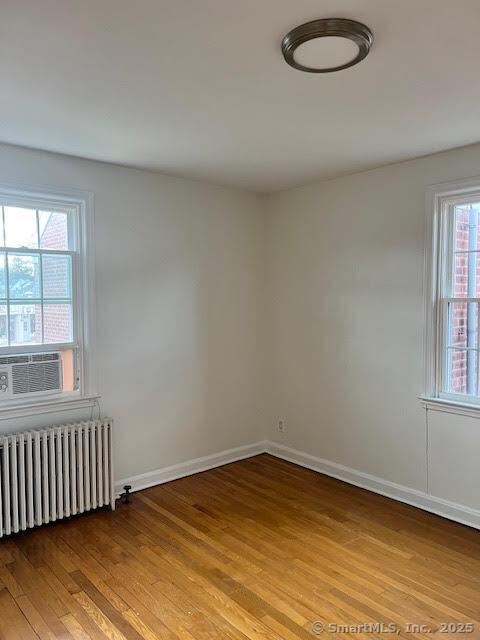 empty room featuring light wood-type flooring, baseboards, and radiator heating unit