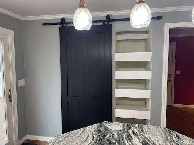 unfurnished bedroom featuring a barn door, wood finished floors, crown molding, and baseboards