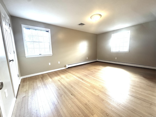 unfurnished room featuring visible vents, plenty of natural light, a baseboard heating unit, and hardwood / wood-style floors