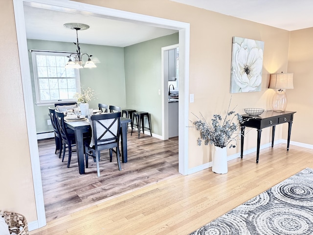 dining room with a notable chandelier, baseboards, baseboard heating, and wood finished floors