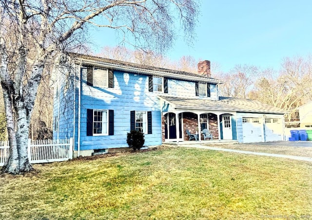 colonial inspired home featuring fence, an attached garage, a chimney, a front lawn, and aphalt driveway